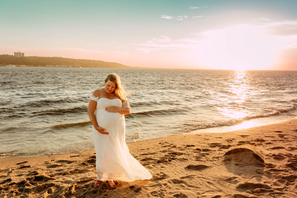 A pregnant woman posing in front of a sunset at Sandy Hook Beach in New Jersey. 